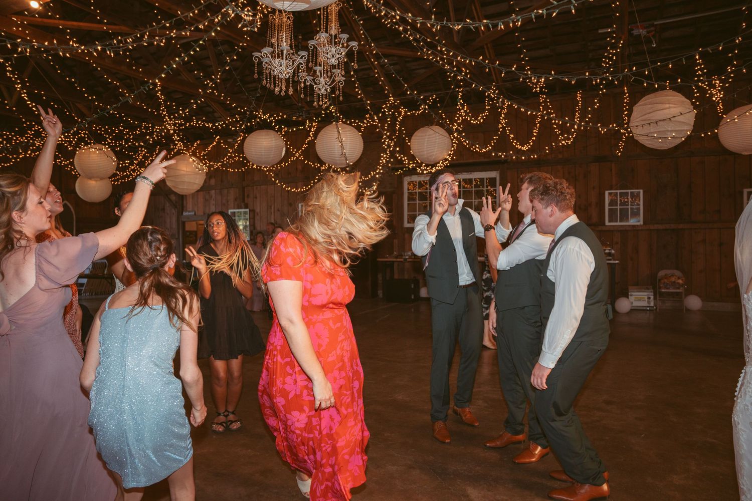 People dancing and celebrating at a barn event with decorative lighting and lanterns.