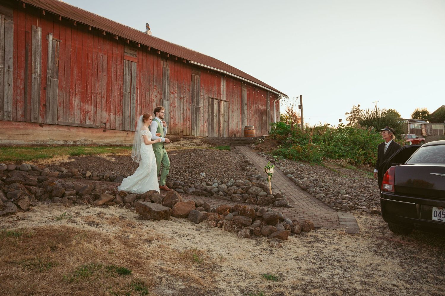 Red barn exterior with gravel pathway and parked cars at sunset.