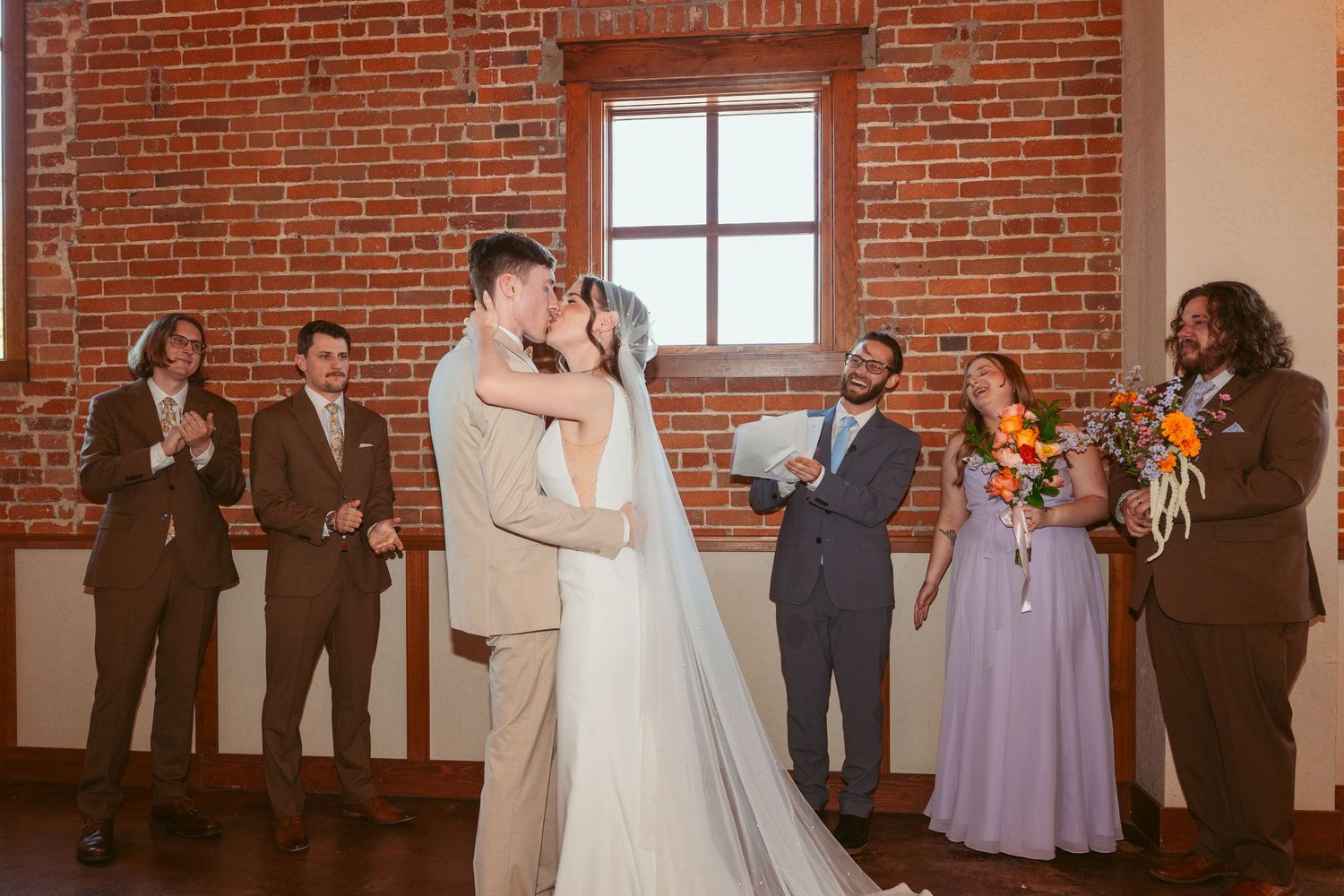 Wedding guests seated in rows watching ceremony in industrial brick venue with warm lighting.