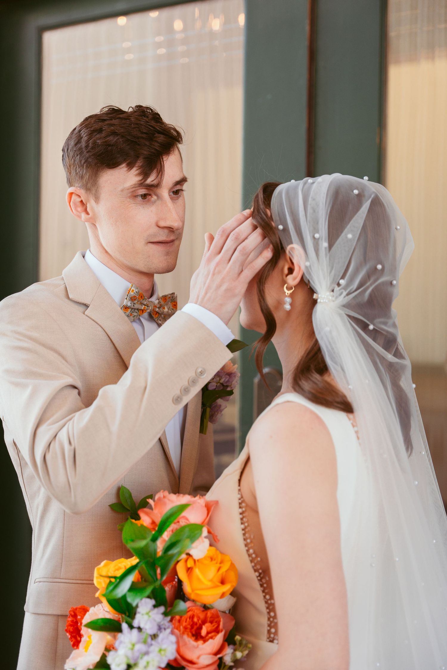 Wedding couple in beige and white sharing sweet moments with colorful floral bouquet.
