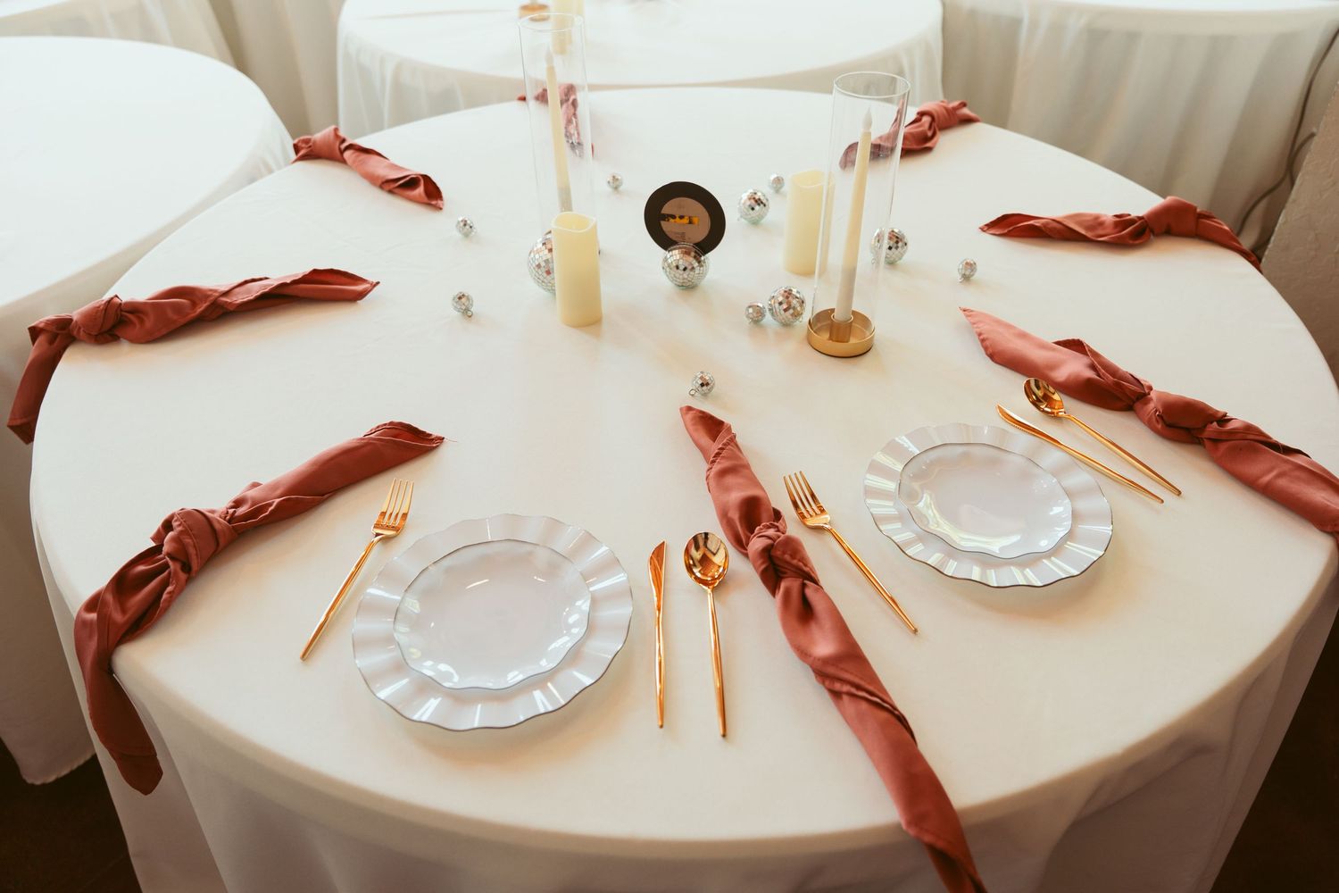 White tablecloth reception setup with burgundy napkins and gold place settings.