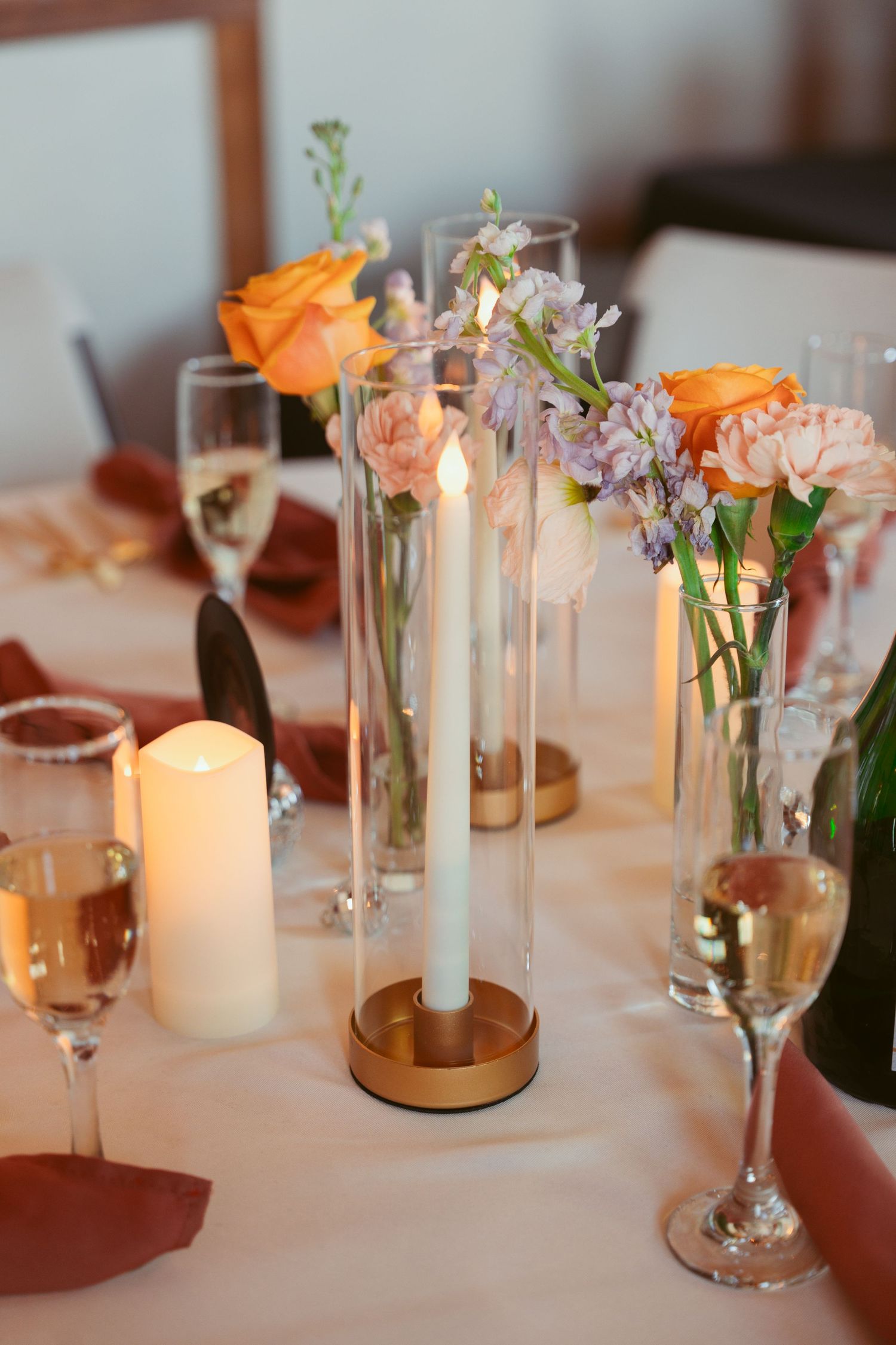 Wedding reception table with tall glass vases holding orange roses and delicate pink flowers.