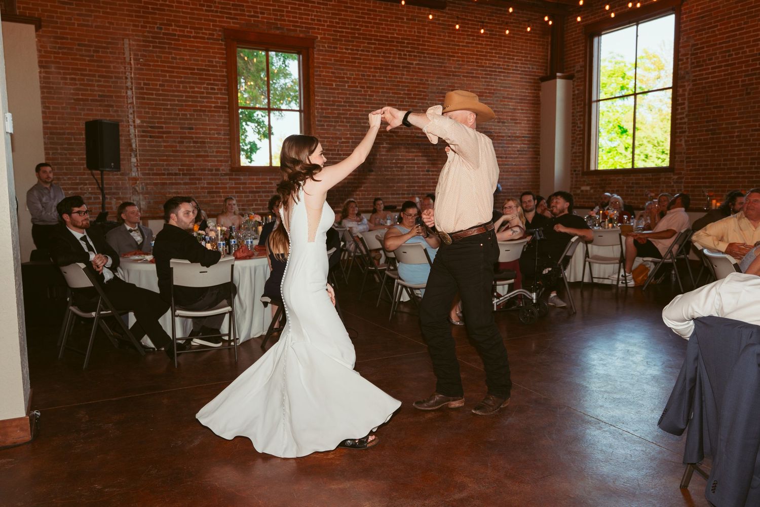 Dancers execute an energetic spin move on the wooden dance floor of a brick-walled reception venue.