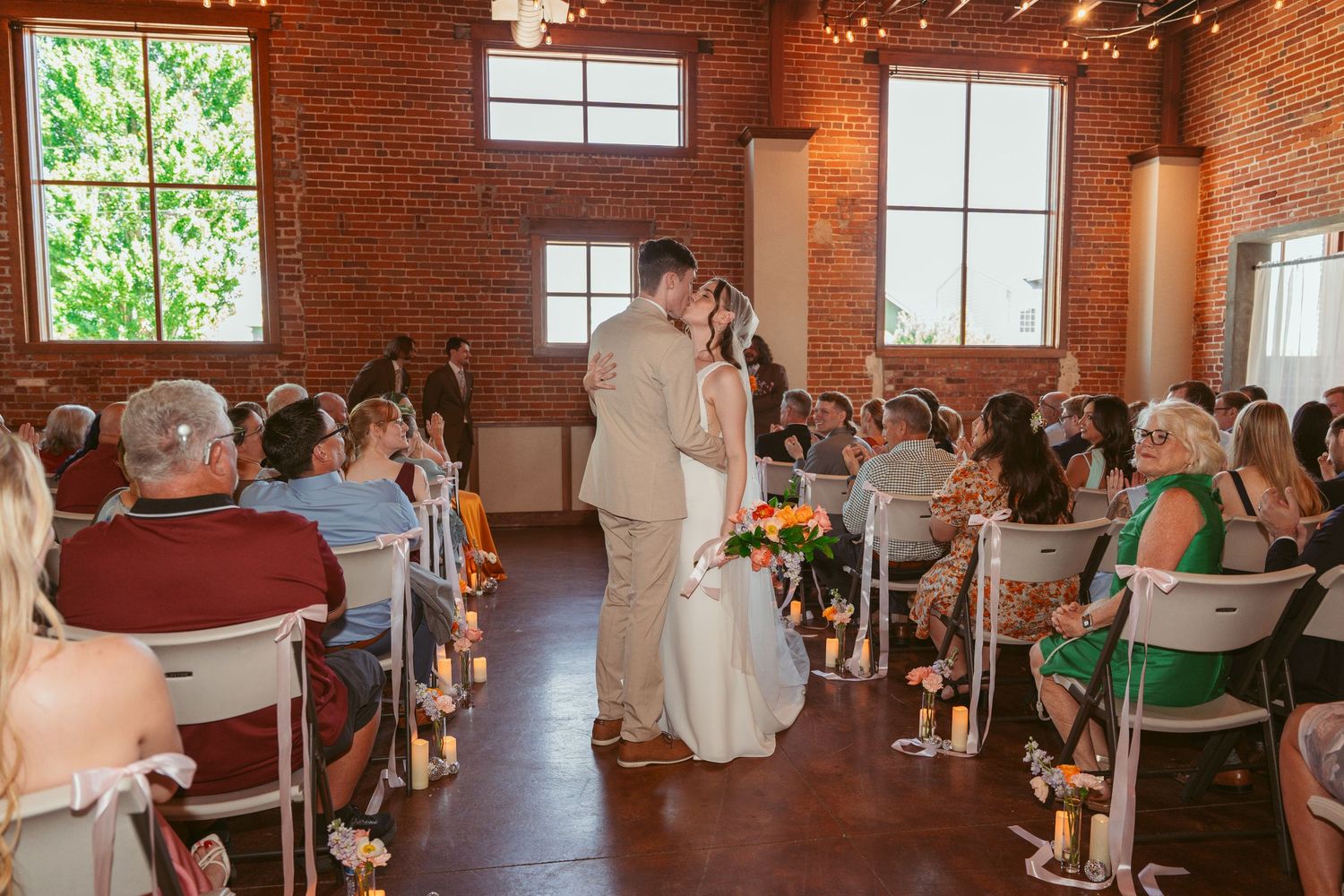 Wedding reception space with exposed brick walls and rows of guest seating.