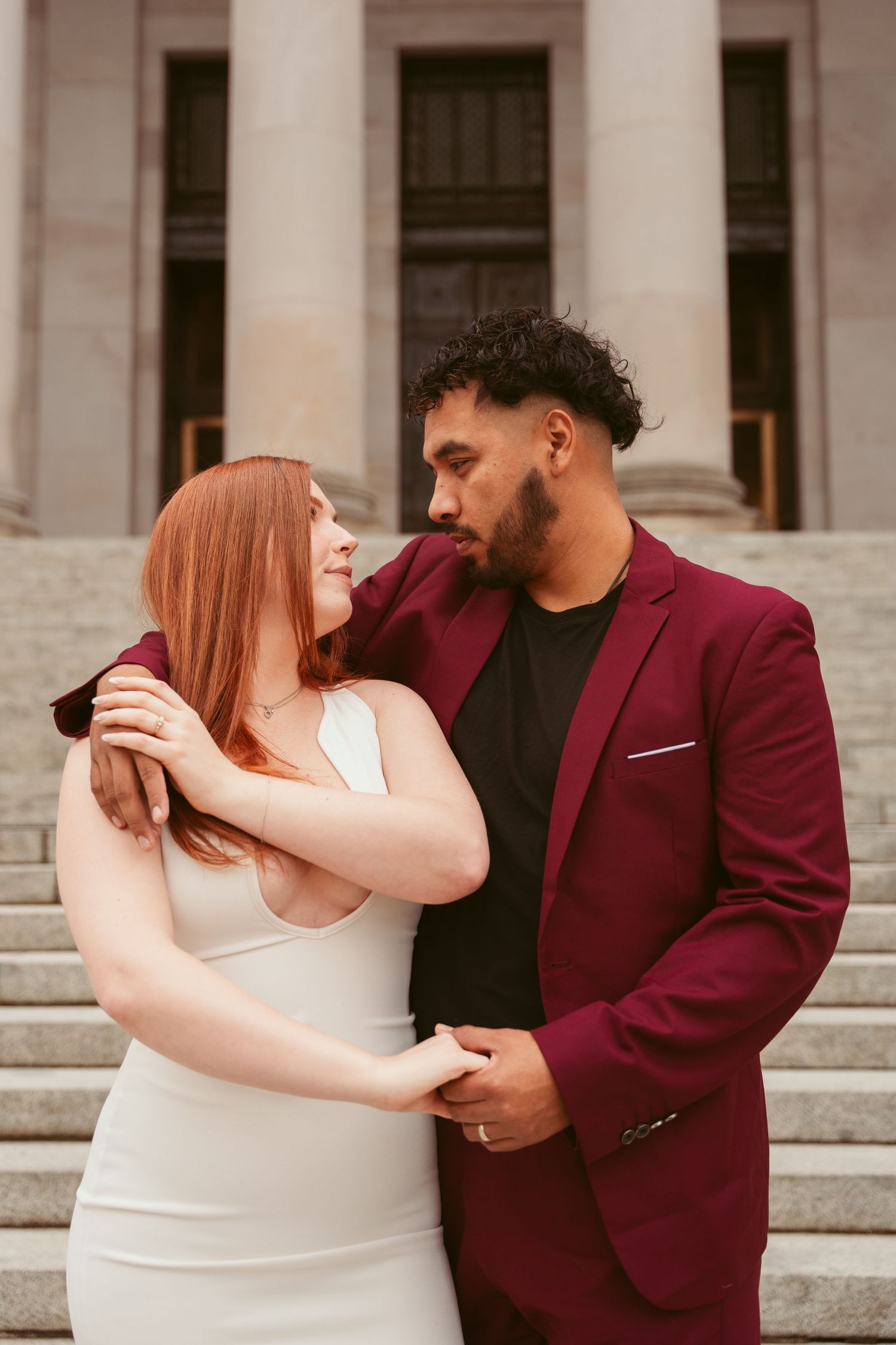 Couple in formal attire sharing romantic moments on marble steps of a building.