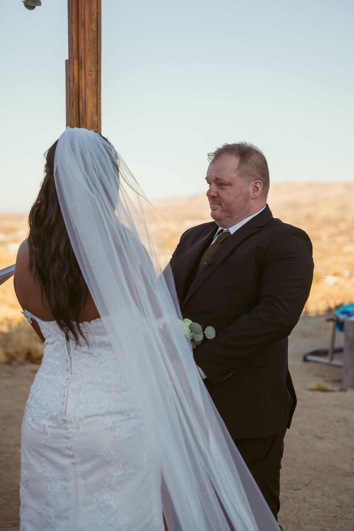 Wedding ceremony moments captured in a desert setting with wooden posts and mountains in background.