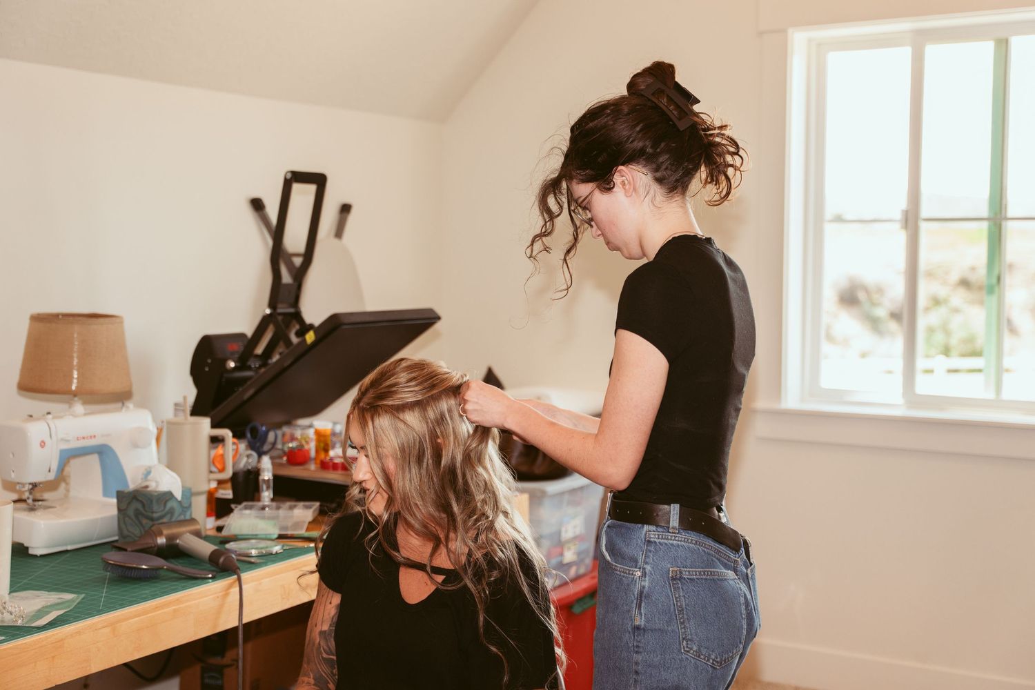 Hair styling session in a bright room with beauty supplies and equipment on wooden table.