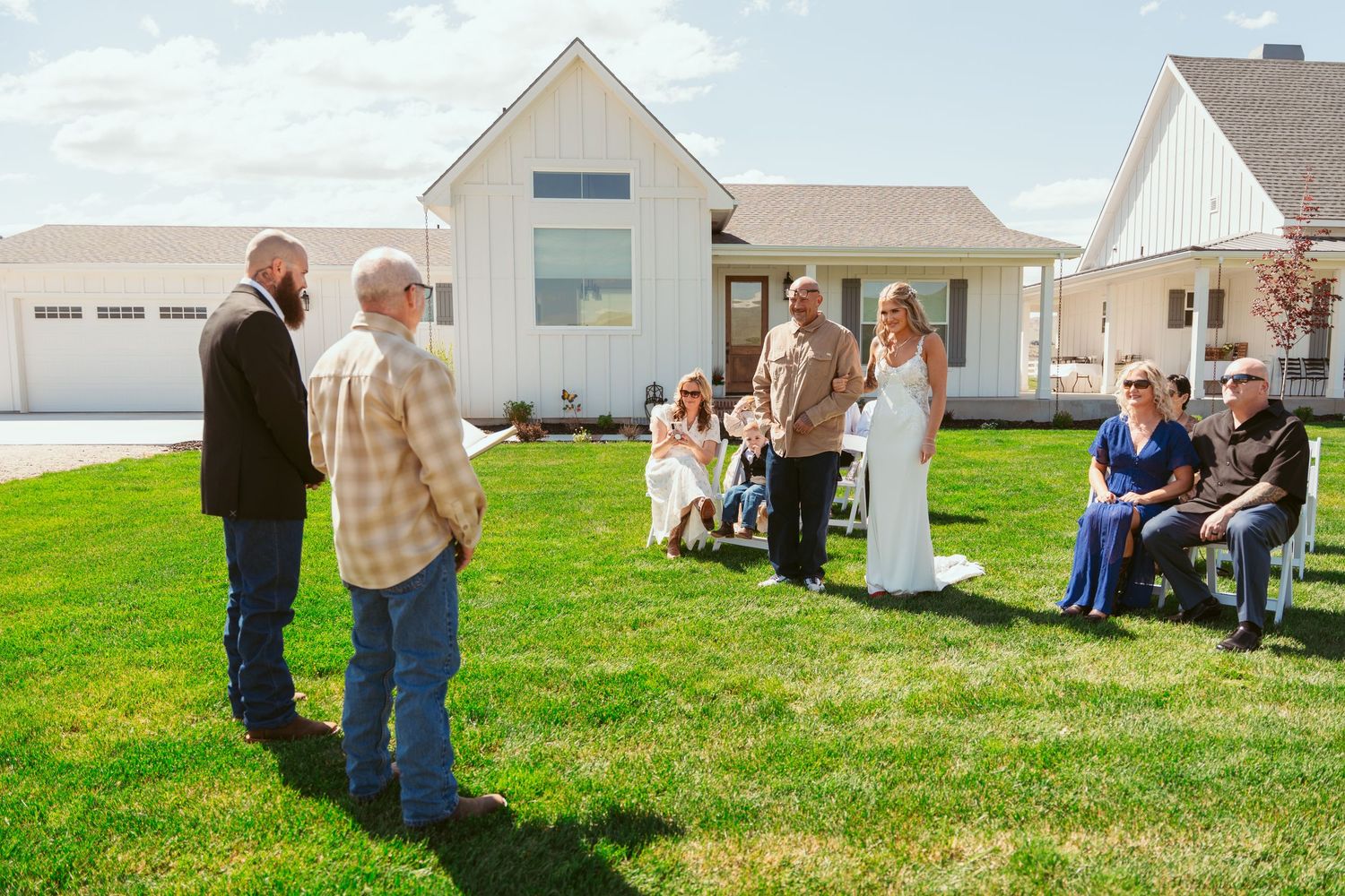 Wedding ceremony guests seated on white chairs on a grassy lawn with mountains in the background.