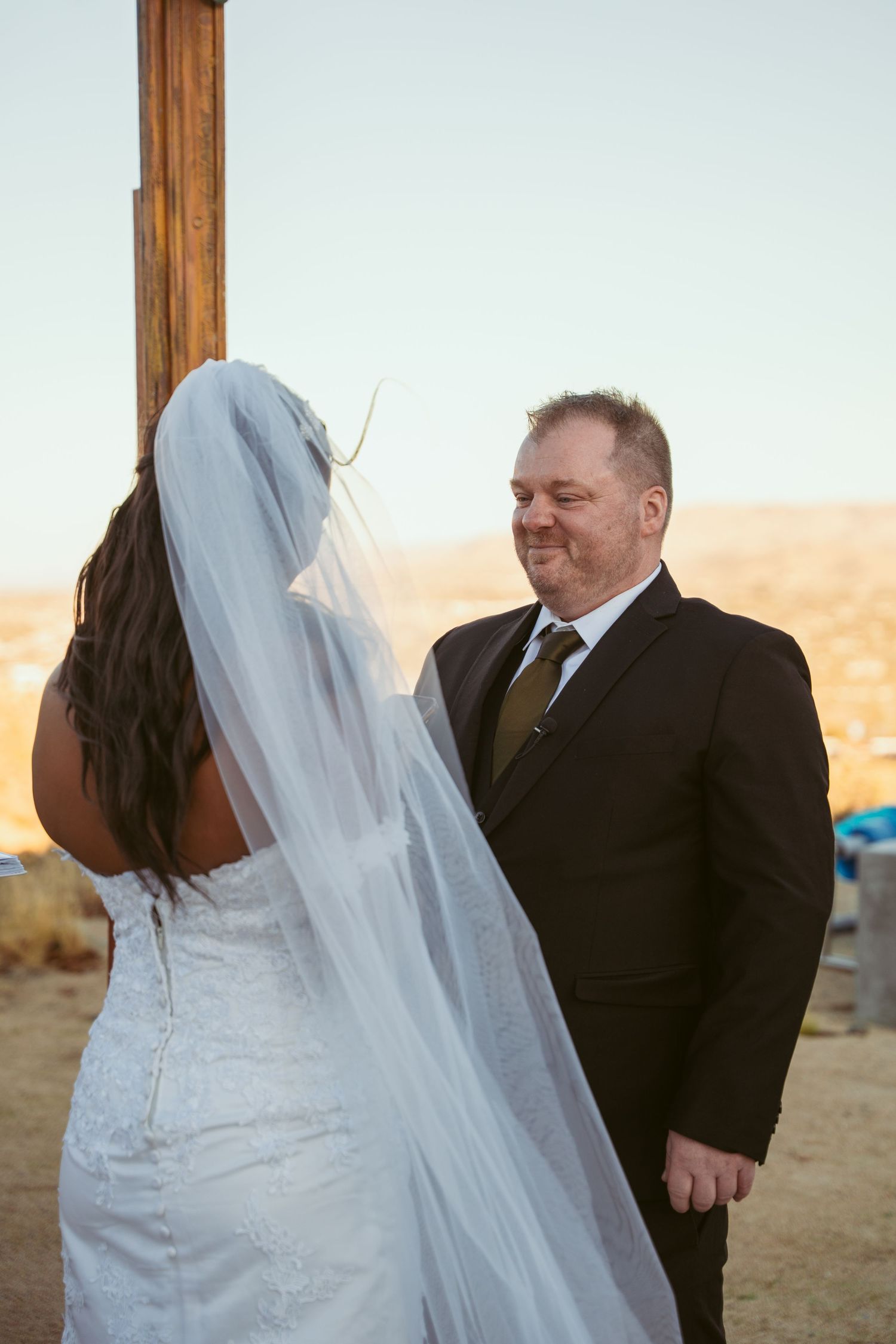 Intimate moment during desert wedding ceremony under wooden arch at sunset.