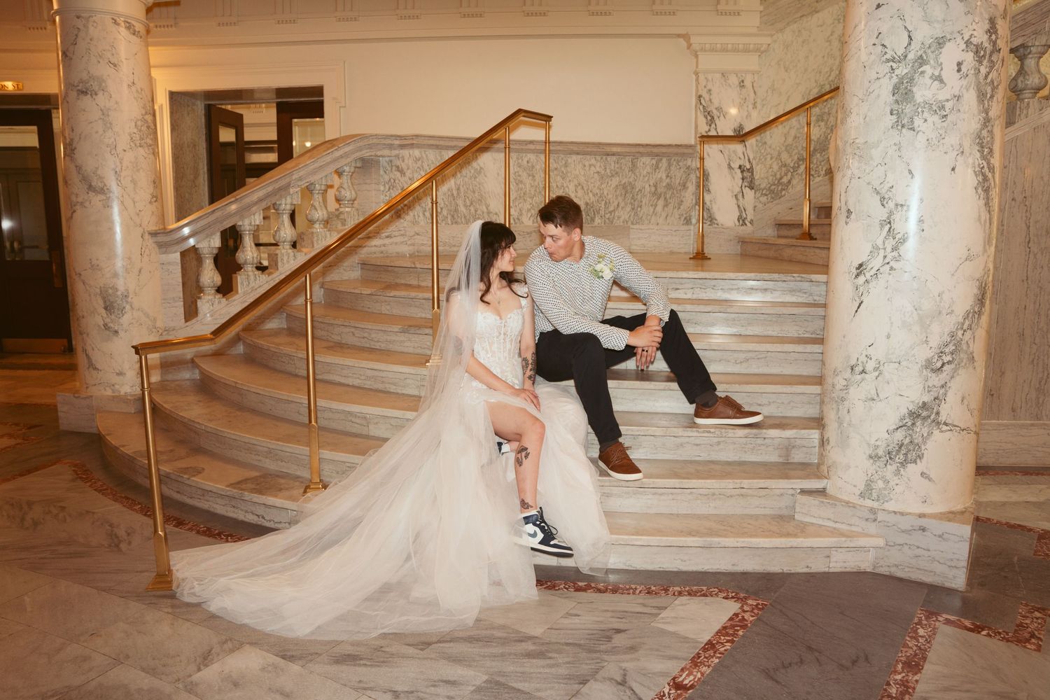 Elegant marble staircase with ornate details serves as backdrop for wedding photos.
