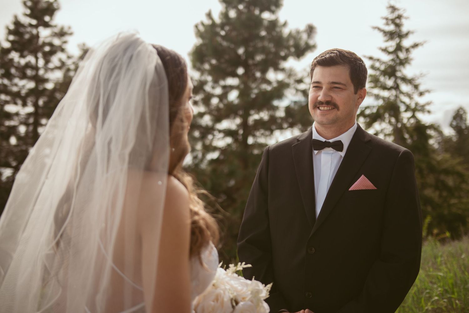 A wedding couple shares a moment outdoors with evergreen trees in the background.