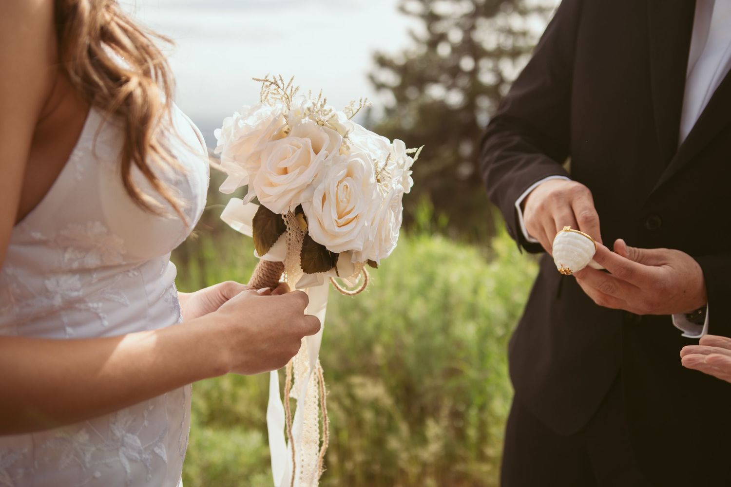 Close-up details of a wedding ceremony with white roses and hands exchanging vows.
