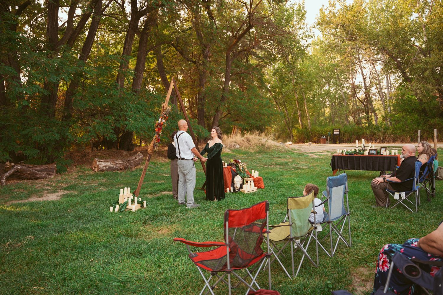 Outdoor gathering with folding chairs set up on grass near wooded area at dusk.