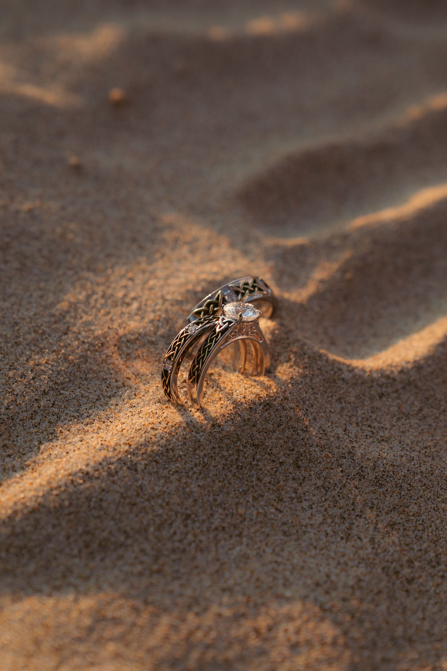 Wedding rings nestled in beach sand catching golden sunset light.