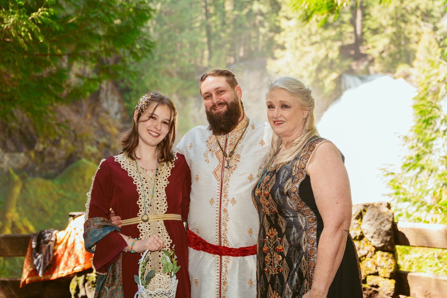 Wedding party members in renaissance attire pose together in a sunlit forest clearing.