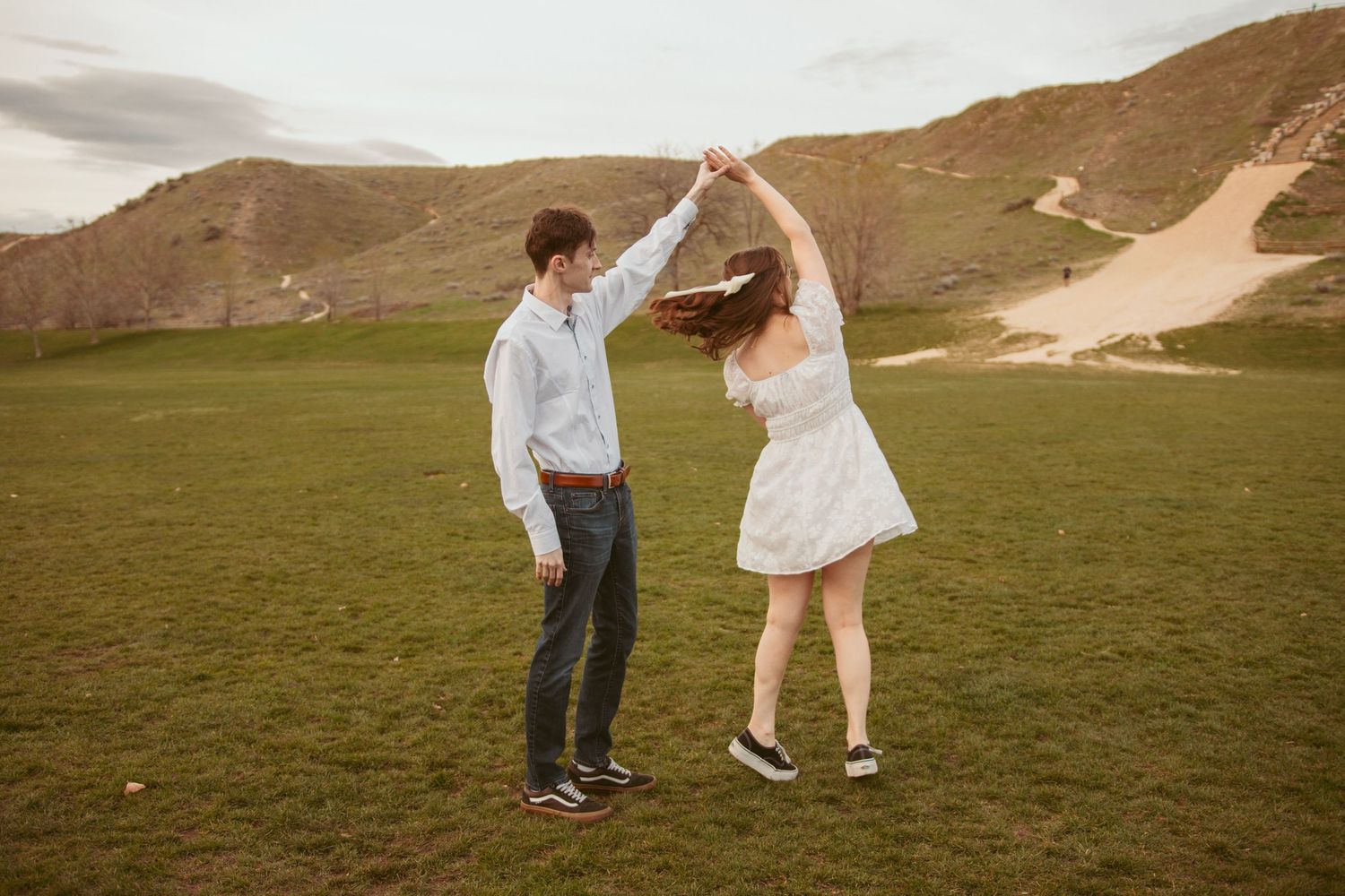 Couple dancing together on green hillside during sunset engagement session.