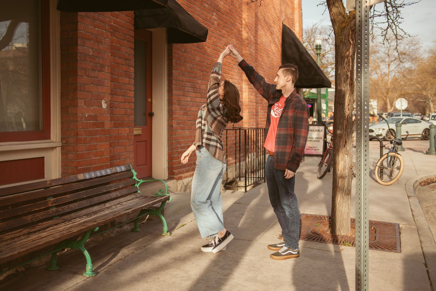 A couple walks together along a brick building sidewalk on a sunny day.