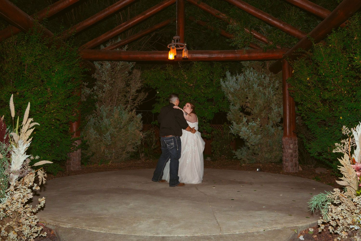 Outdoor wedding venue decorated with string lights and rustic wooden beams at dusk.