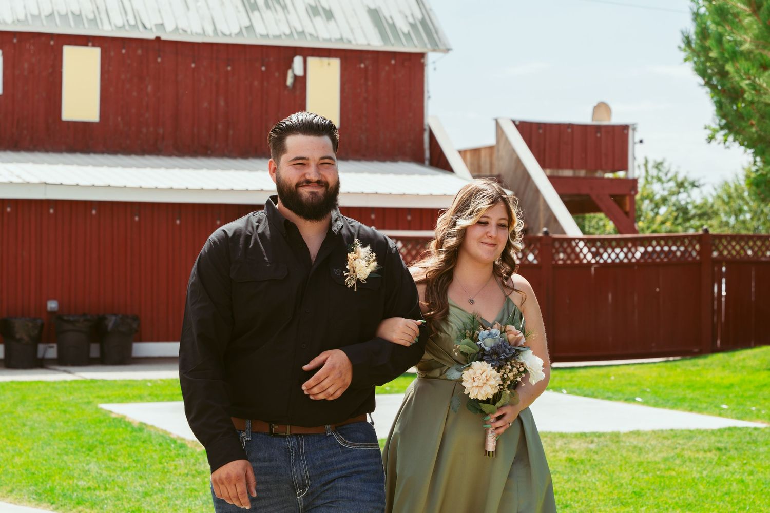 Red barn provides backdrop for outdoor wedding celebration on sunny day.