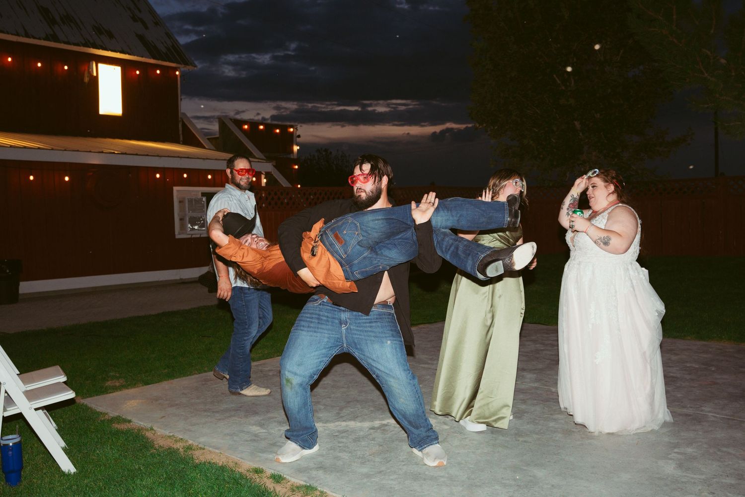 Wedding guests participate in group dances on an outdoor patio at night.