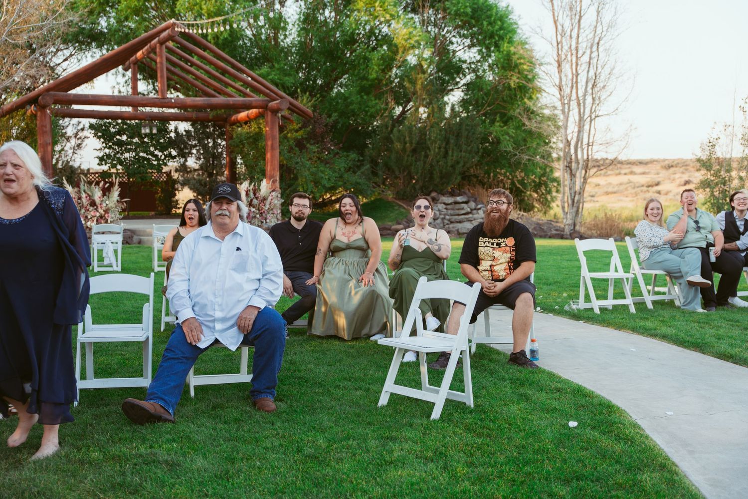 Outdoor wedding ceremony setup with white chairs on grass lawn in front of rustic barn.