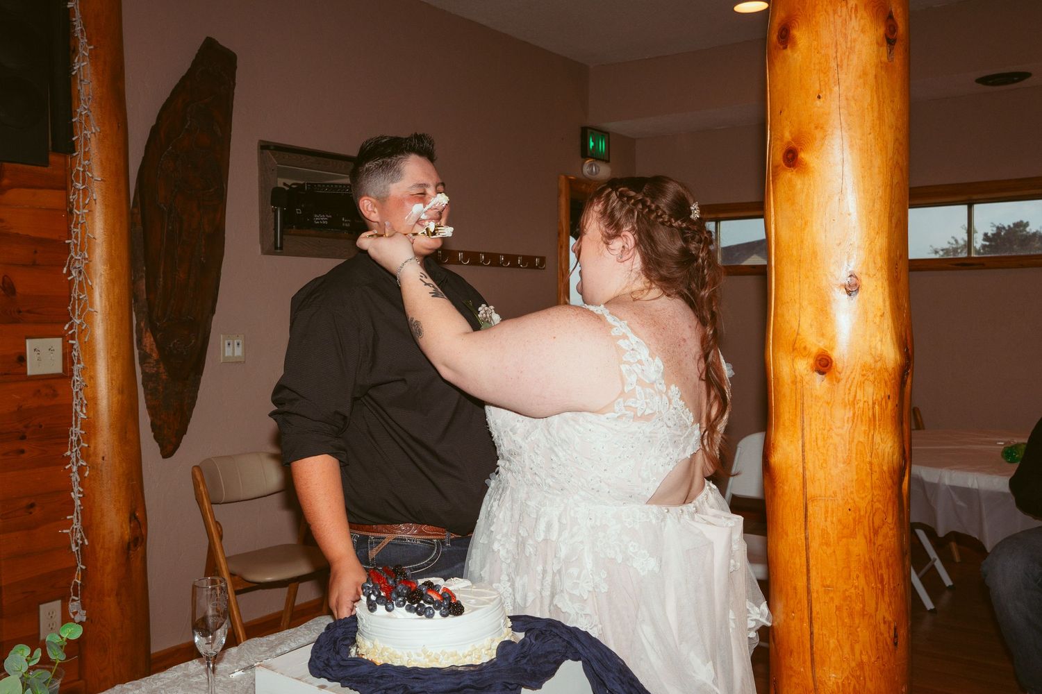 Wedding reception scene with decorative wooden pillars and cake cutting celebration.