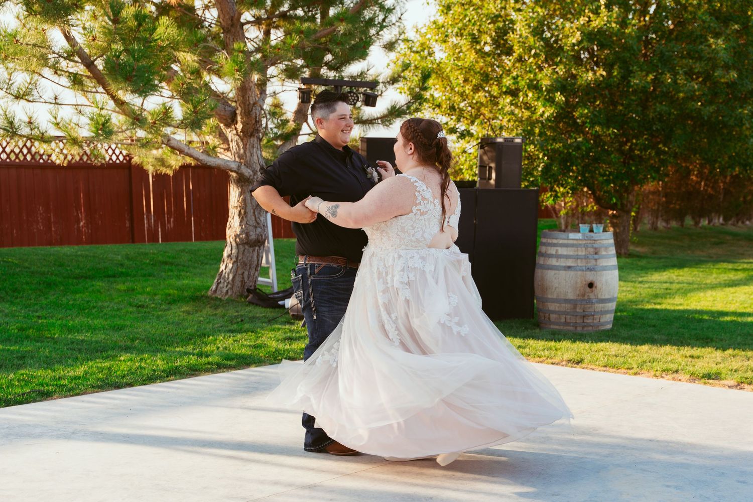 Wedding party members dancing and celebrating on a lawn with trees in the background at sunset.