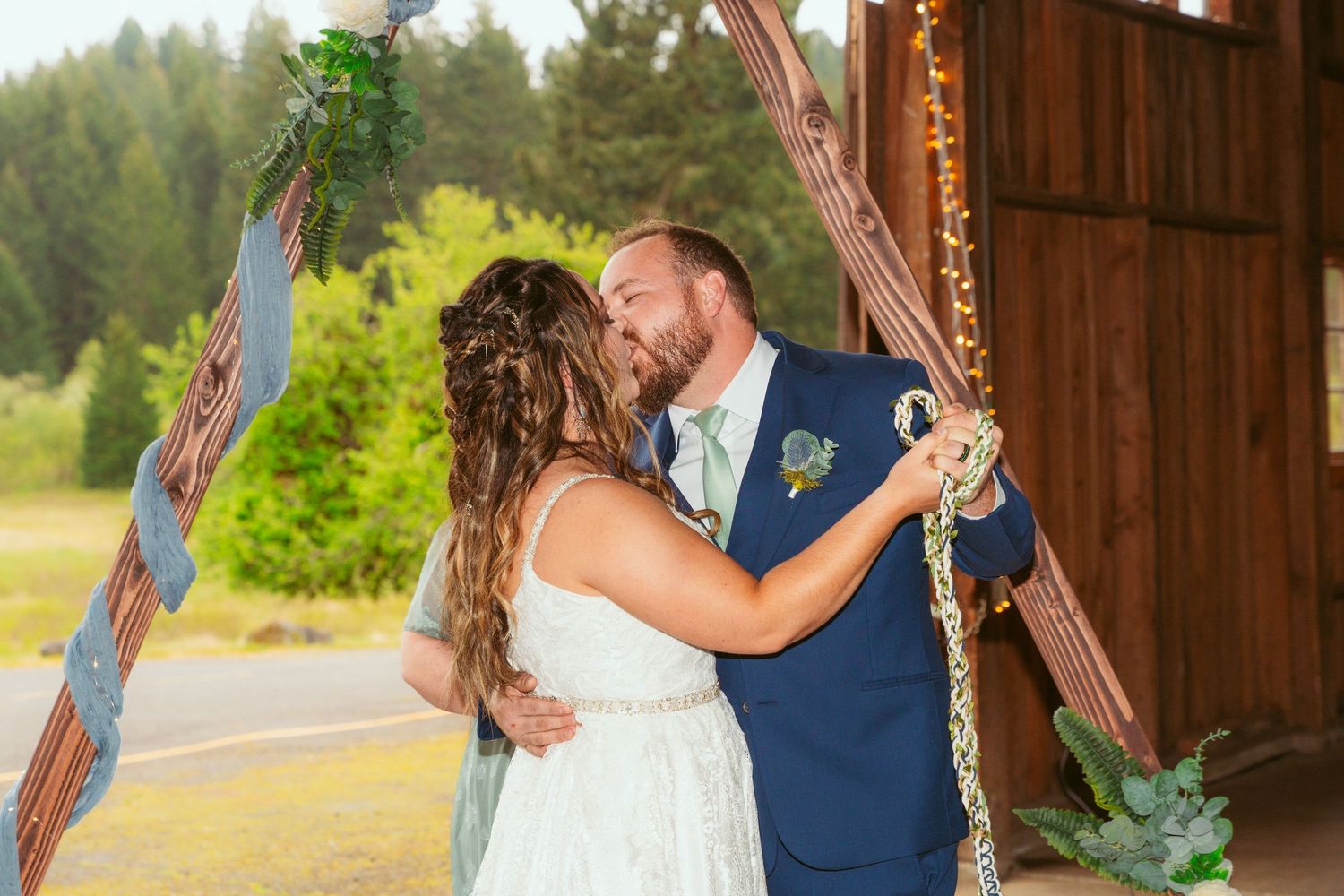 Sunlit barn wedding ceremony with forest visible through open doorway.