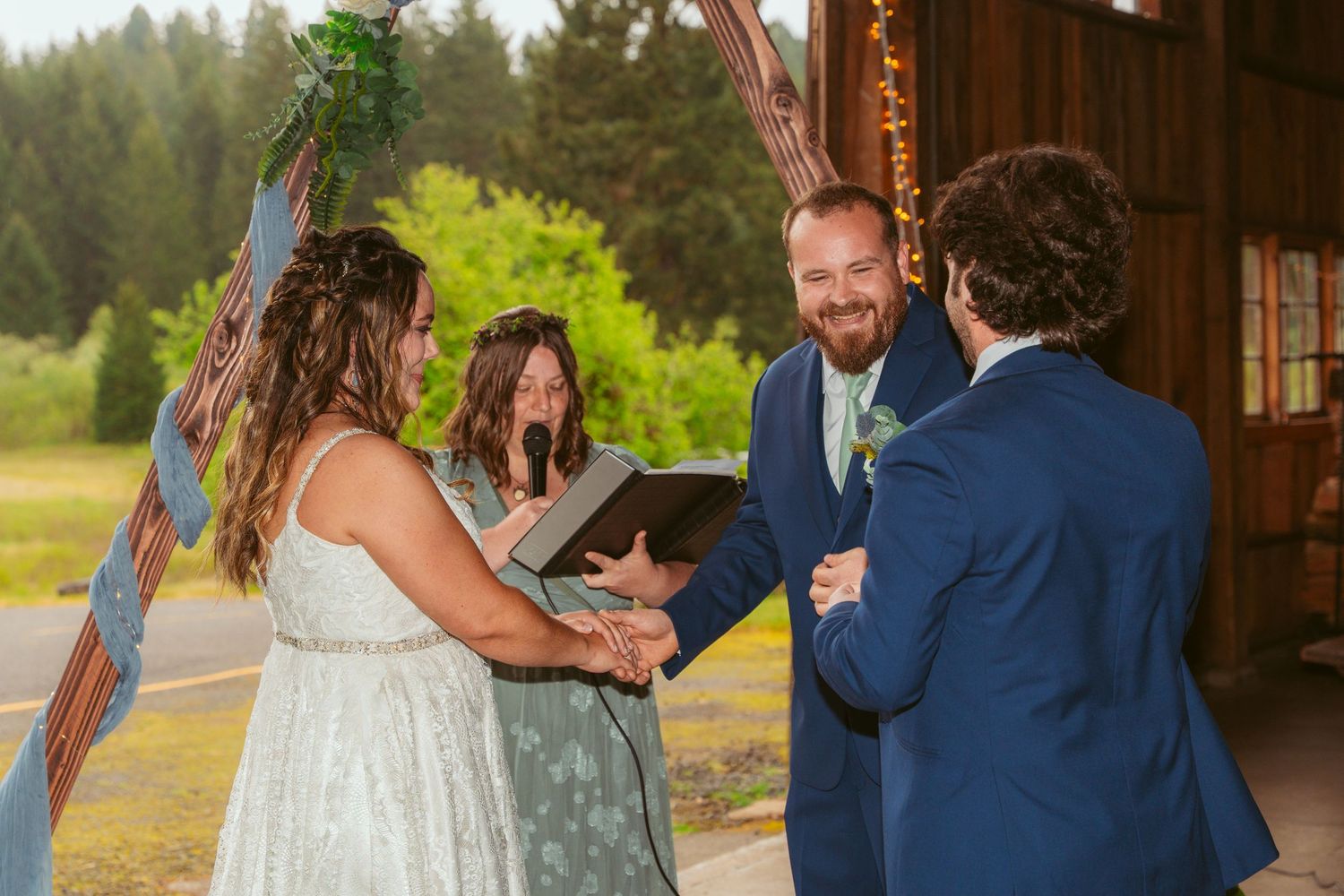 Wedding couple exchanges vows in a rustic barn with forest views through open sides.
