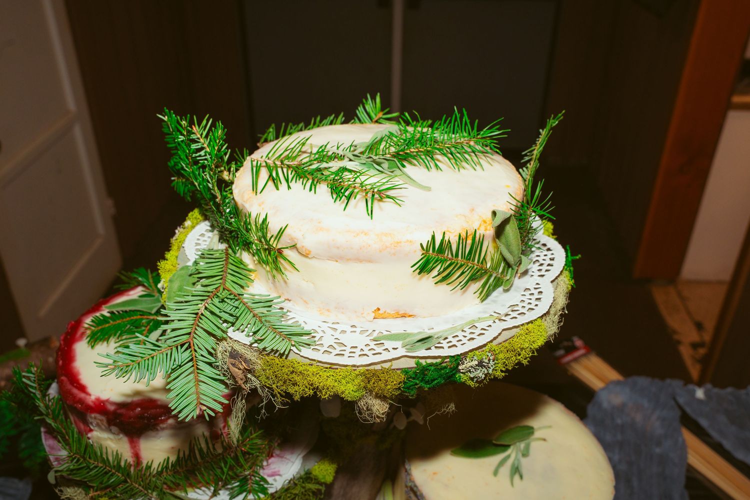 Multi-tiered white wedding cake adorned with fresh evergreen sprigs and delicate decorations.