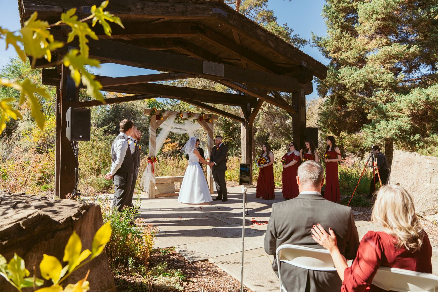 Rustic wedding pavilion decorated with yellow flowers against a blue autumn sky.