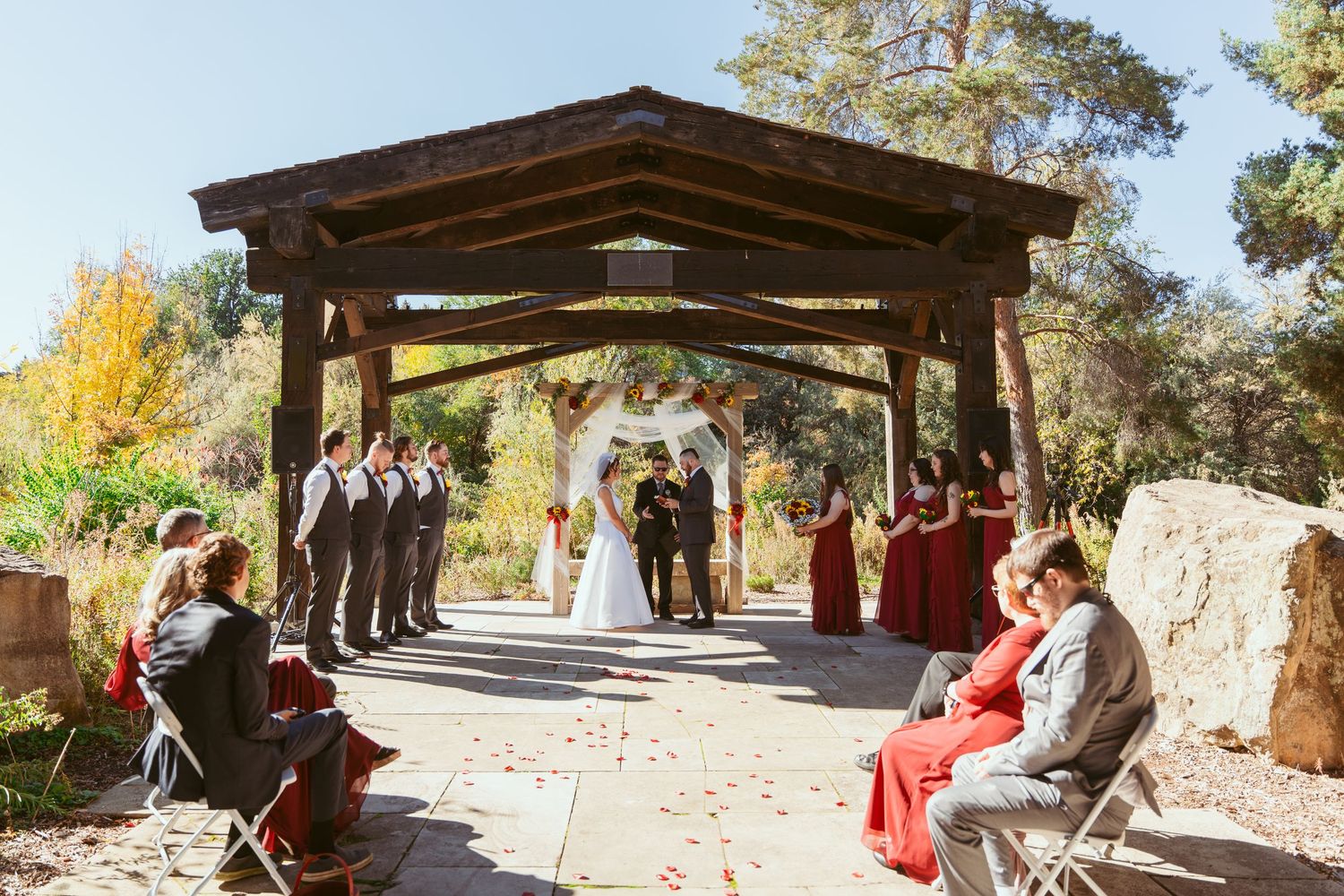 Outdoor wedding venue with wooden pergola and stone pathways surrounded by autumn foliage.