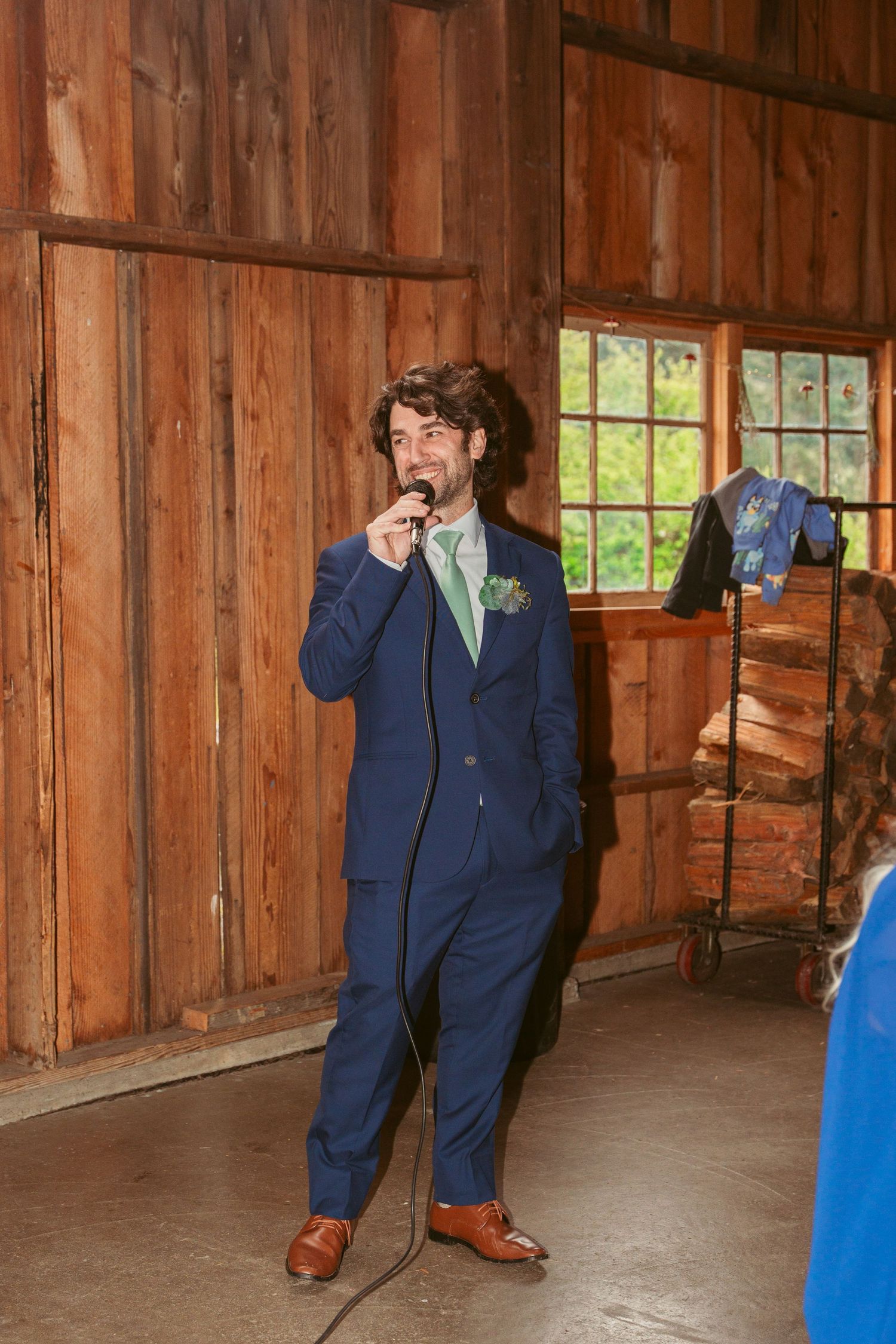 Groomsman in navy suit delivers emotional speech at rustic barn wedding reception.