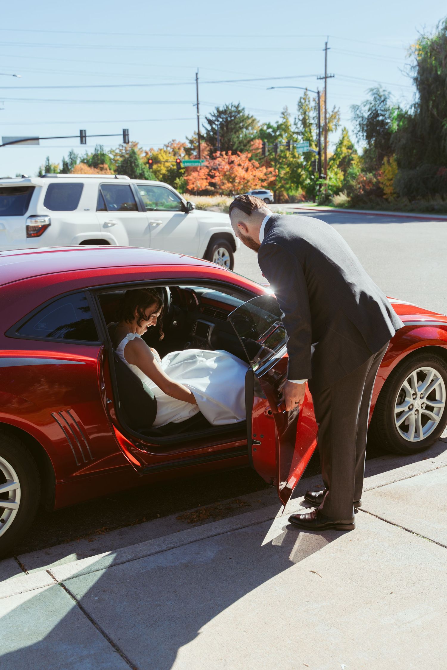 A sunny autumn day wedding scene with a red car and formal attire.
