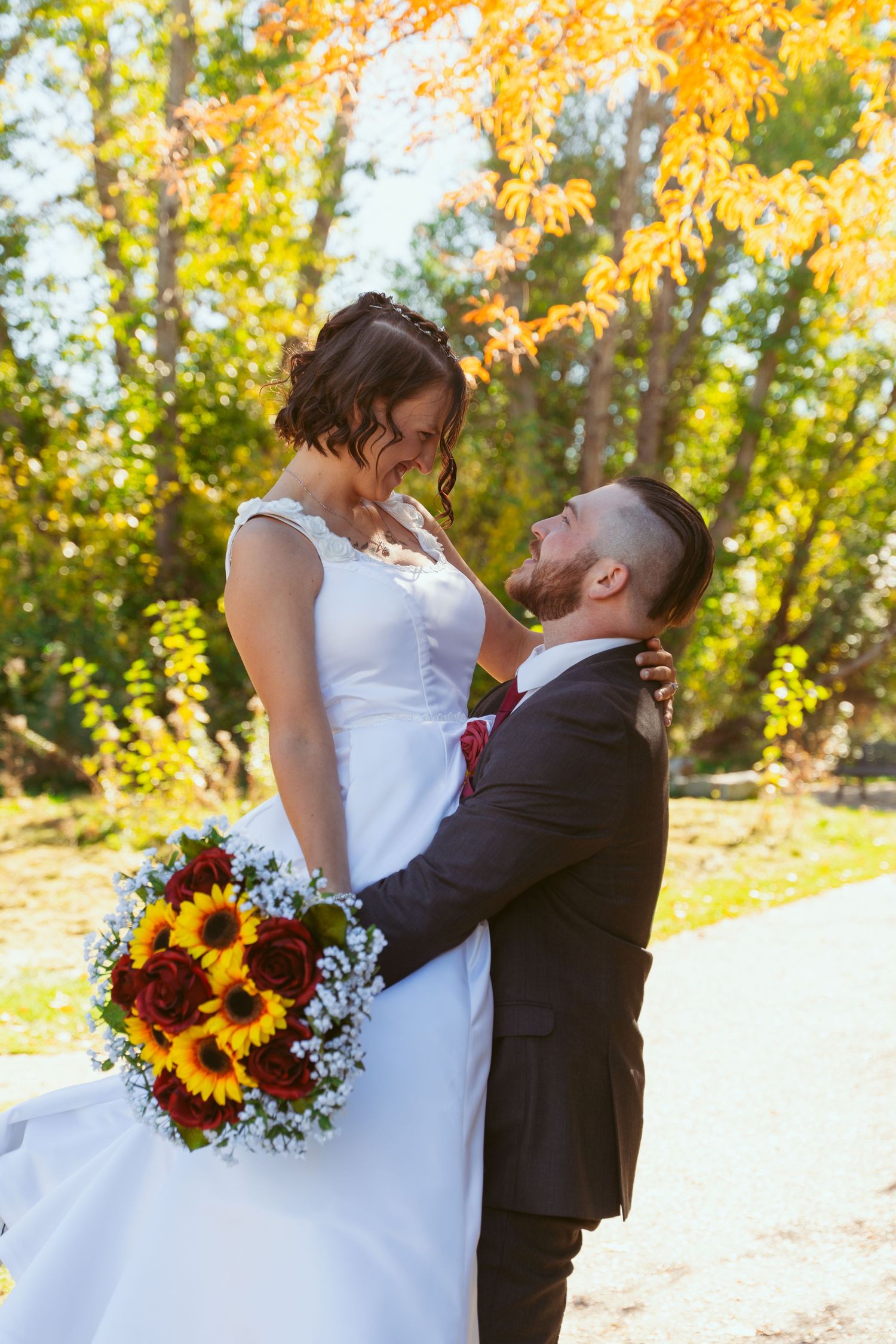 A tender moment between newlyweds with a vibrant sunflower bouquet against autumn trees.