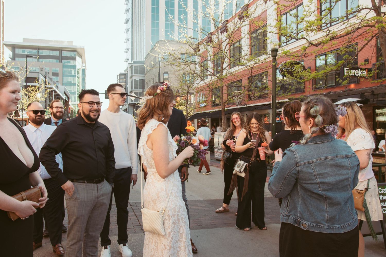 Wedding guests celebrate on an urban street with city buildings in the background.