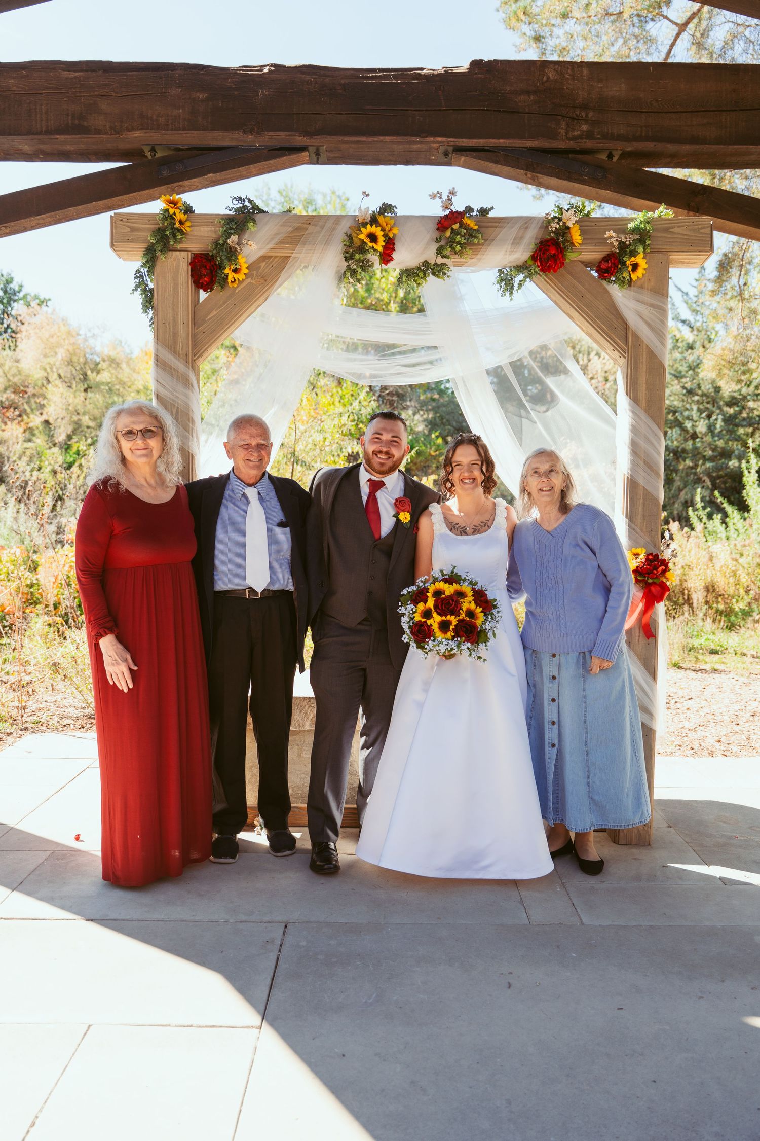Family and wedding party members gather for formal photos under outdoor pavilion.