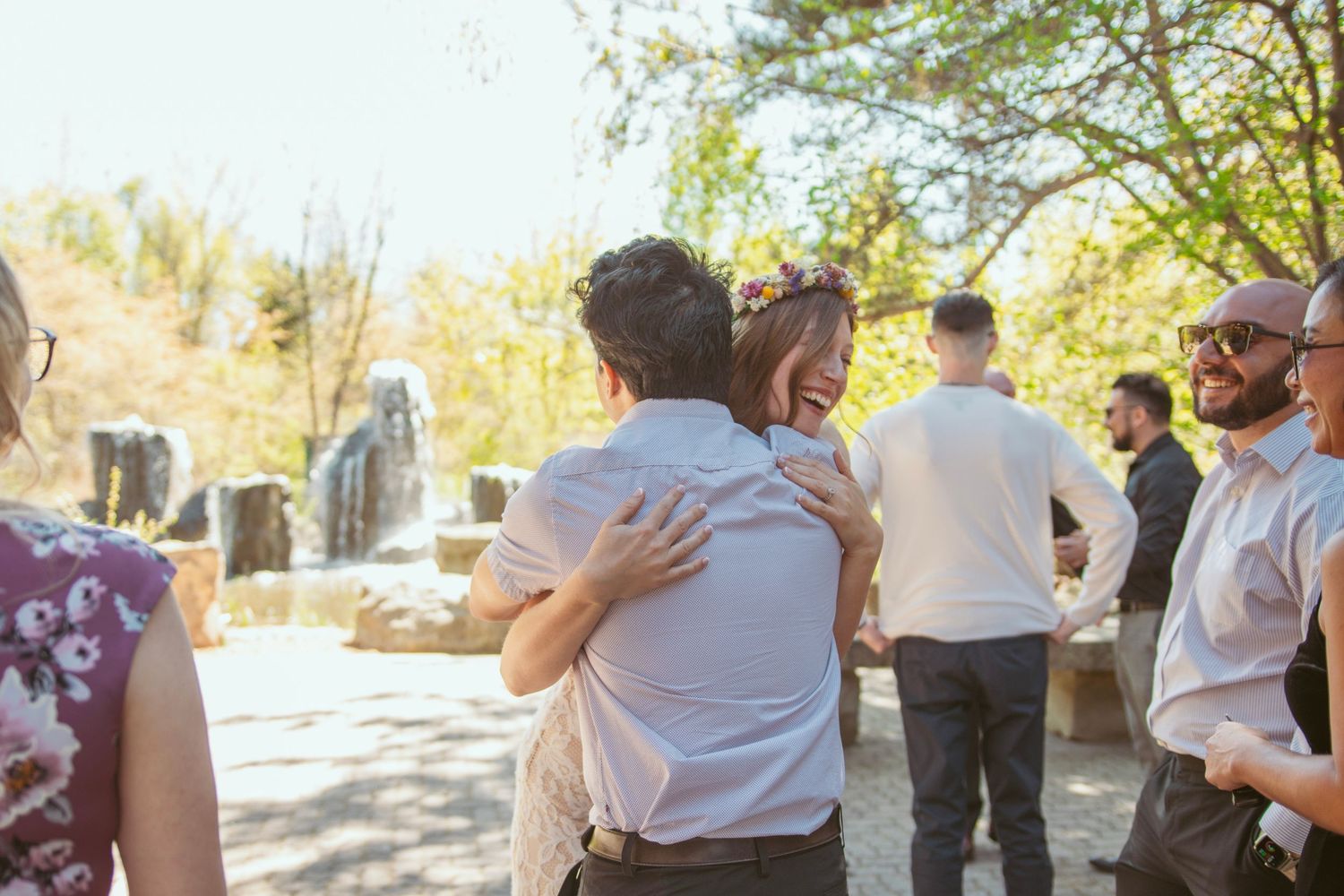 Wedding guests dance together outdoors in front of a colorful graffiti wall at a daytime celebration.