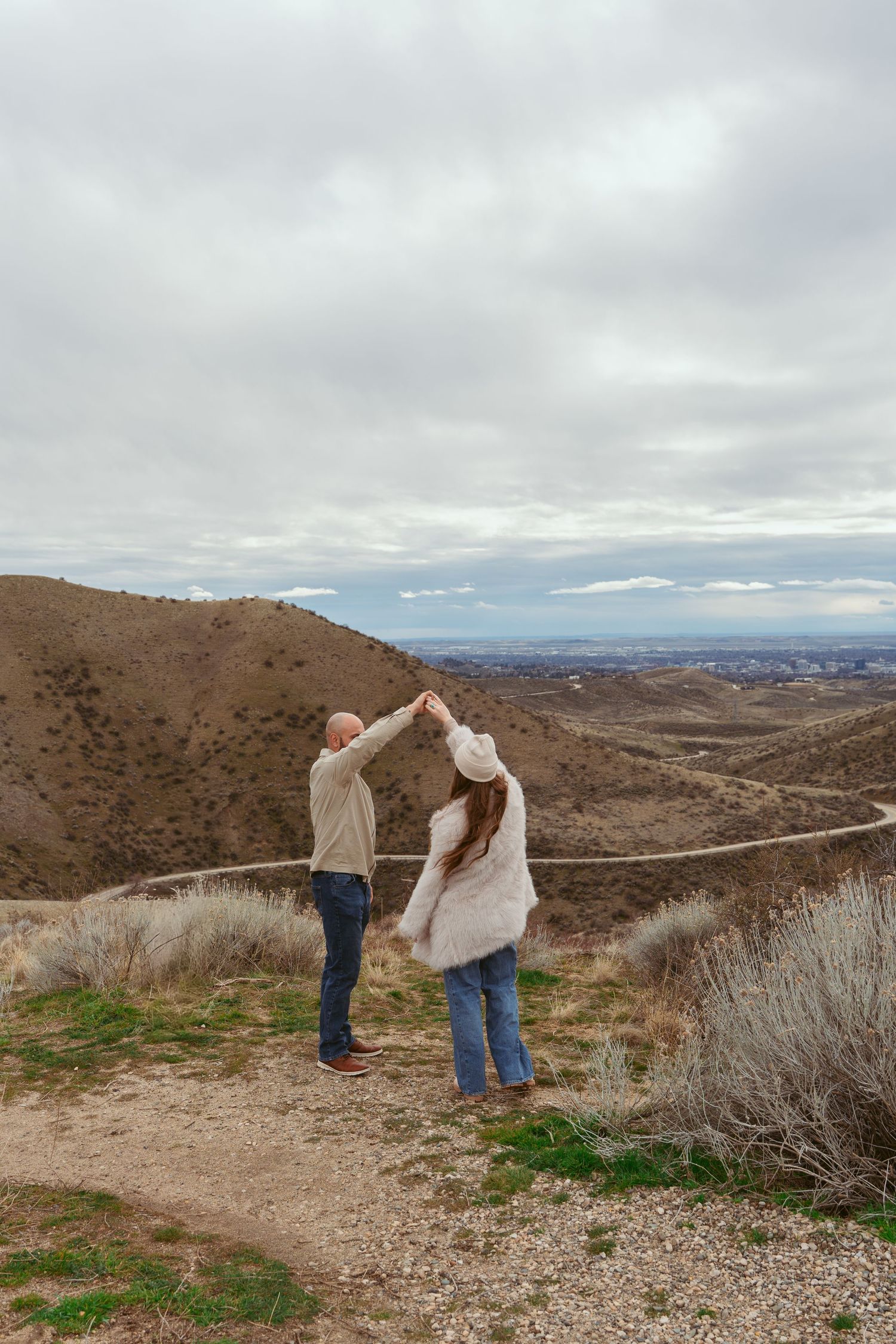 A couple dances together on a mountain trail with scenic valley views in the background.