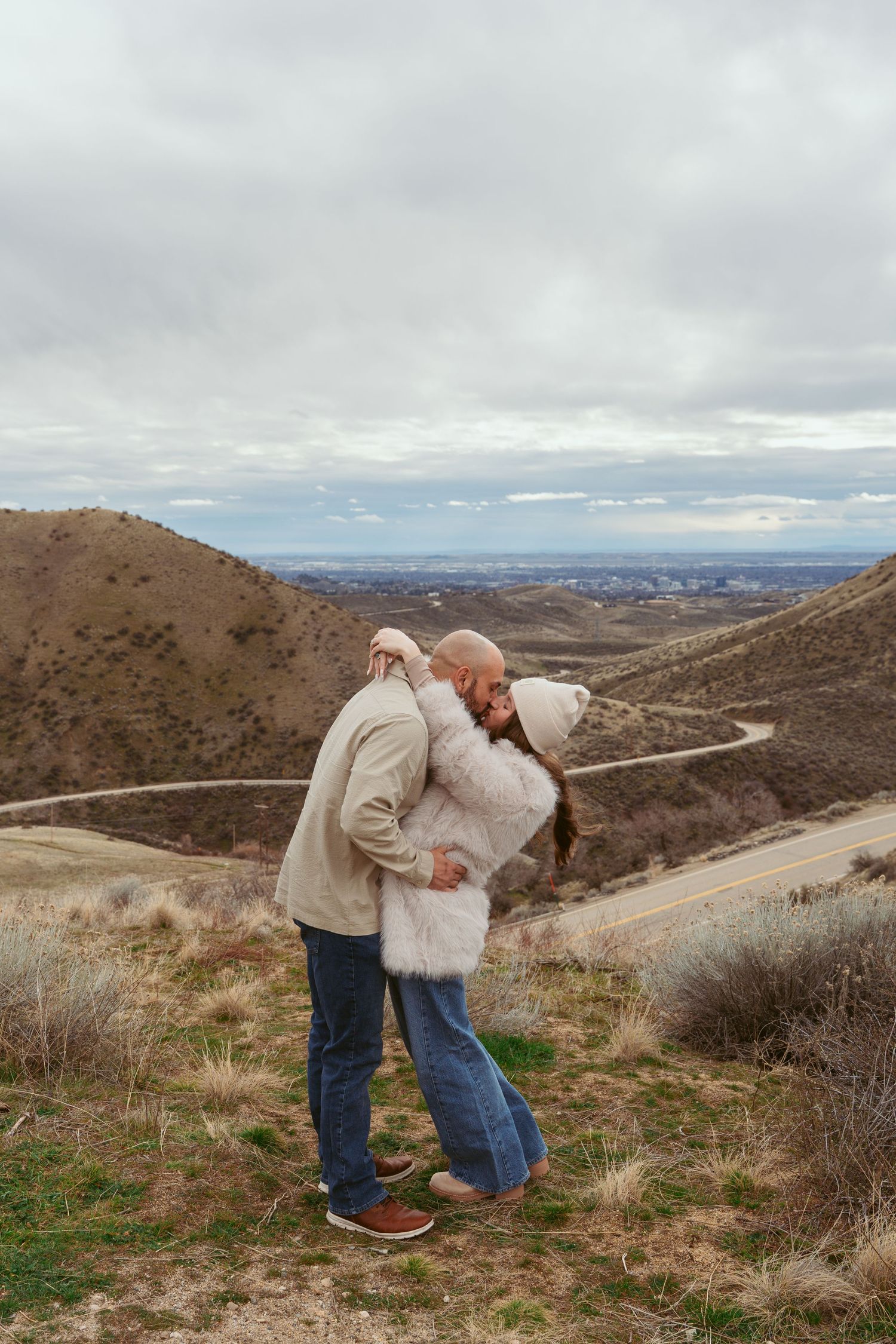 A romantic moment shared between a couple overlooking a winding mountain road on a cloudy day.