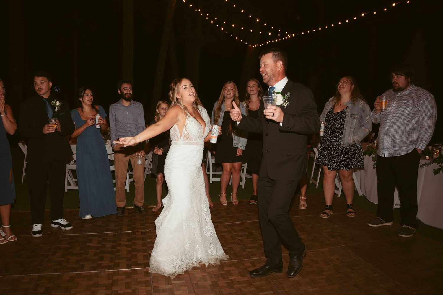 Couples dancing together at a dimly lit outdoor wedding reception.