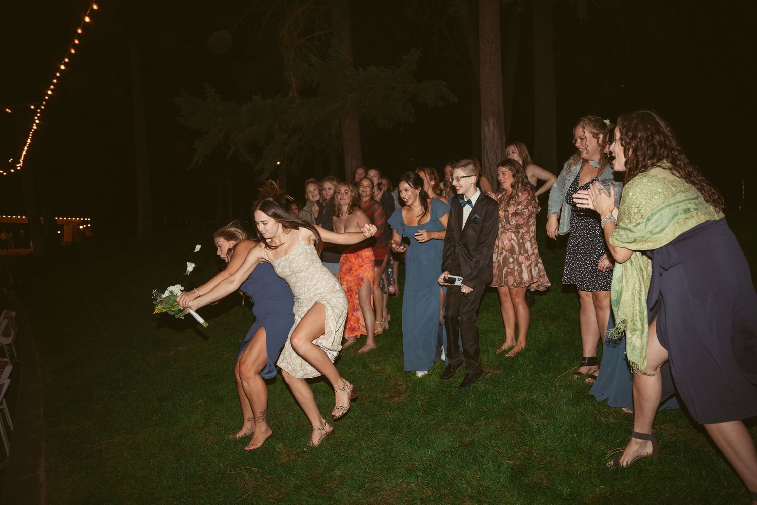 People dancing in a line formation at a nighttime outdoor wedding celebration.