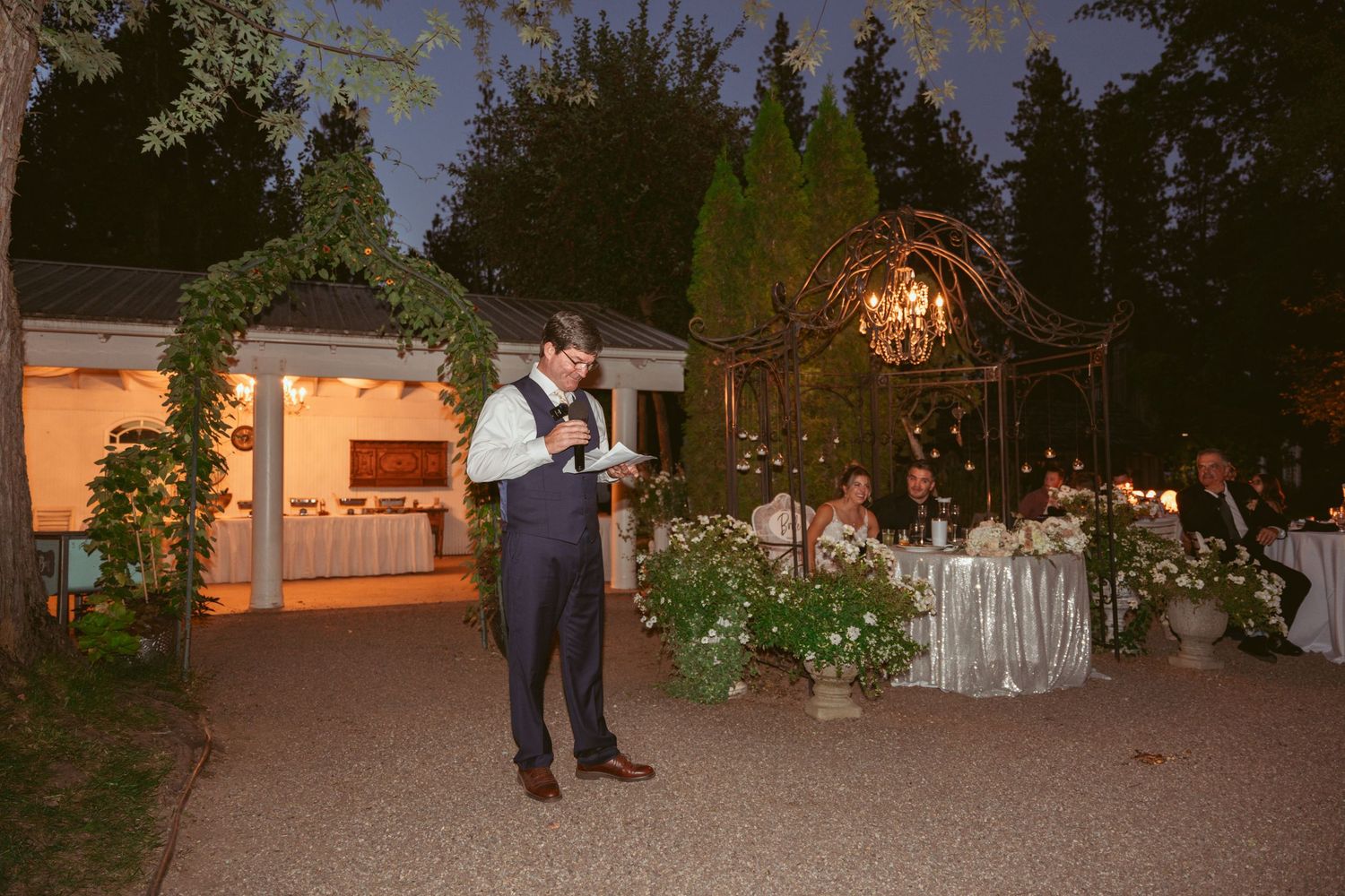 Outdoor wedding reception space at dusk with ambient lighting and decorated tables.