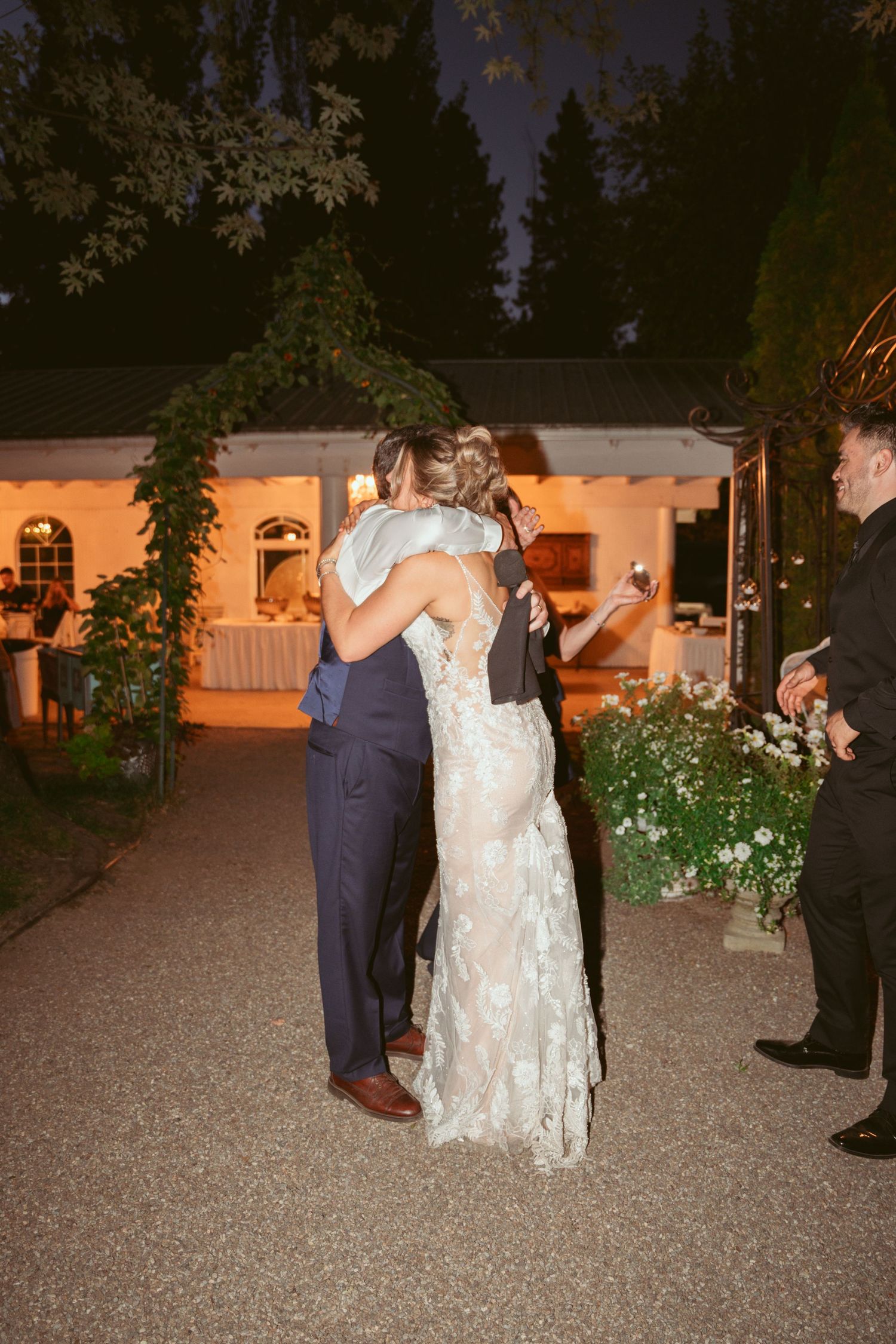 Couples slow dancing on a gravel patio during an evening wedding reception.