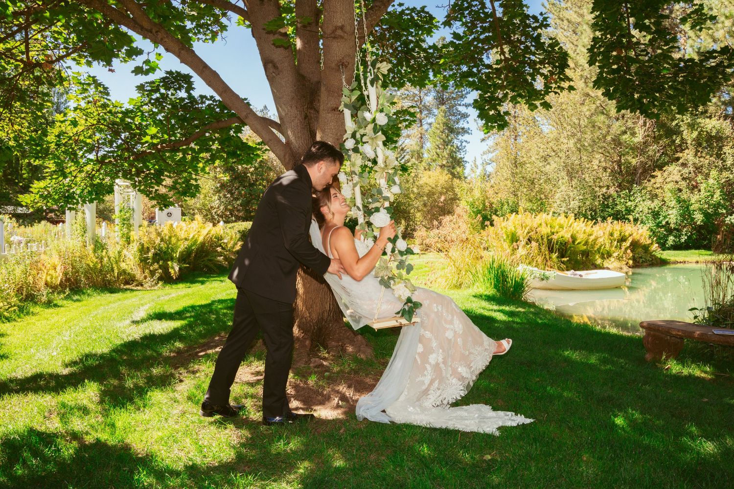 Wedding couple embracing under a large tree in a sunny garden setting.