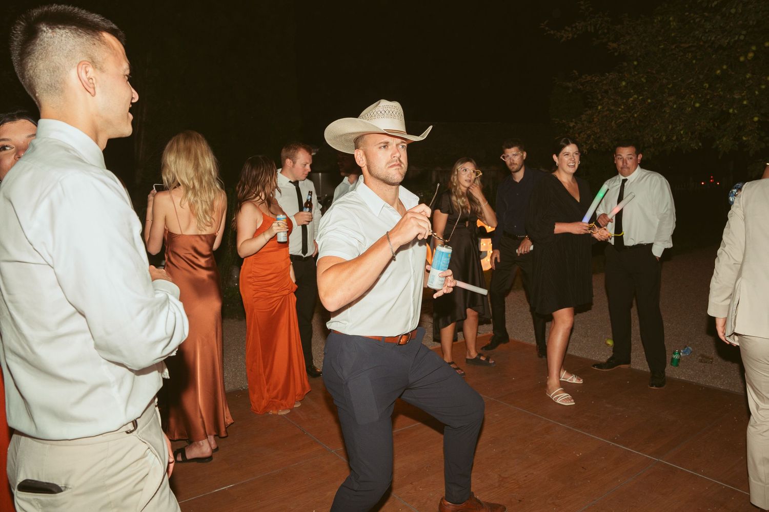 Guest in cowboy hat performs dance moves at outdoor wedding reception.