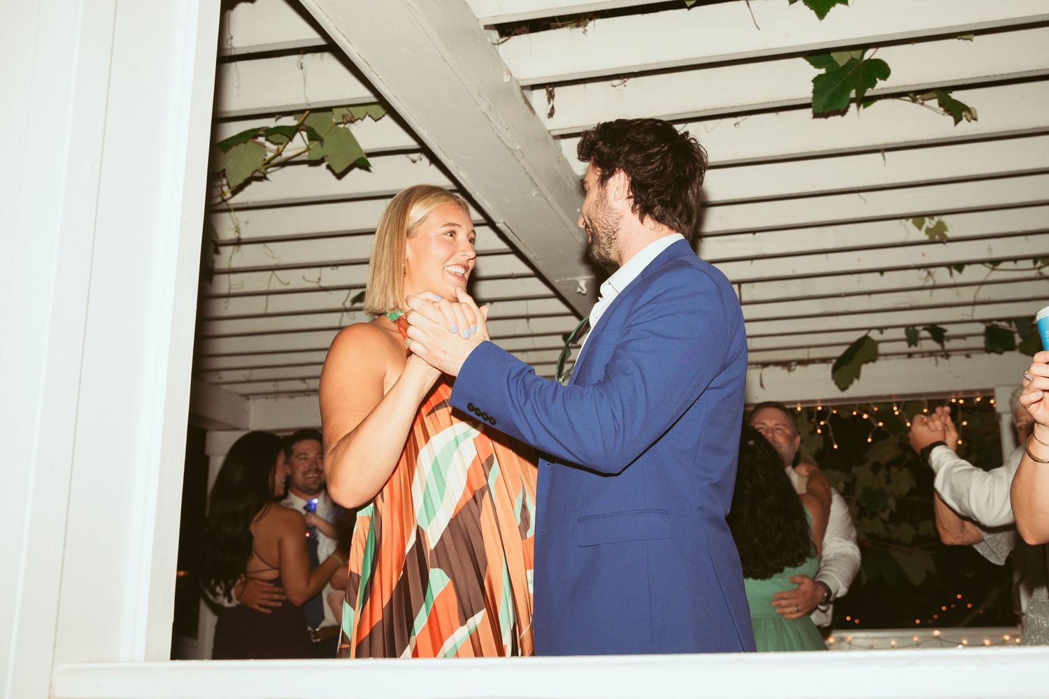 Couple dancing together under a white pergola with hanging lights.