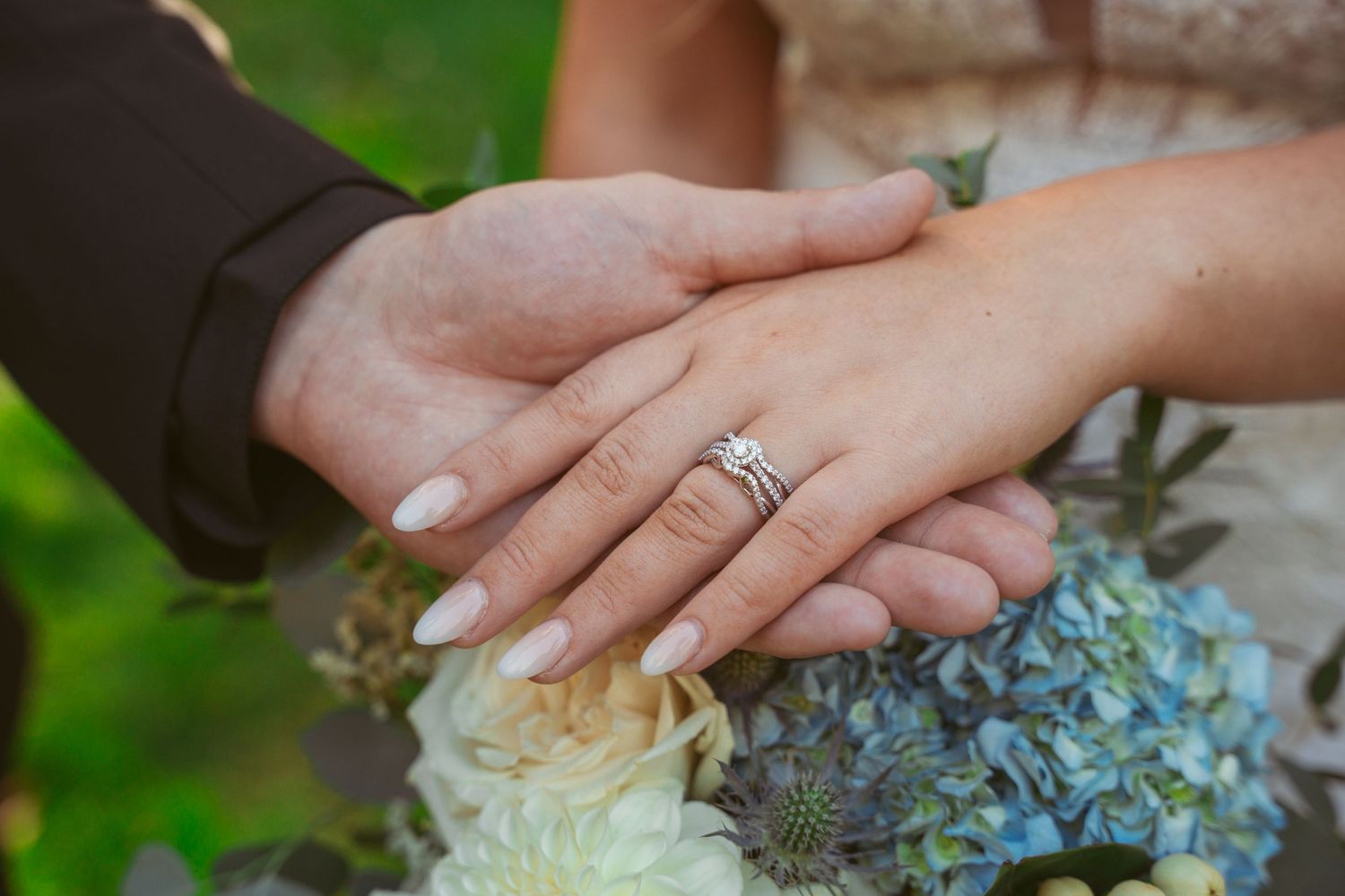 Wedding bouquet details featuring blue hydrangeas and white roses with hands displaying rings.