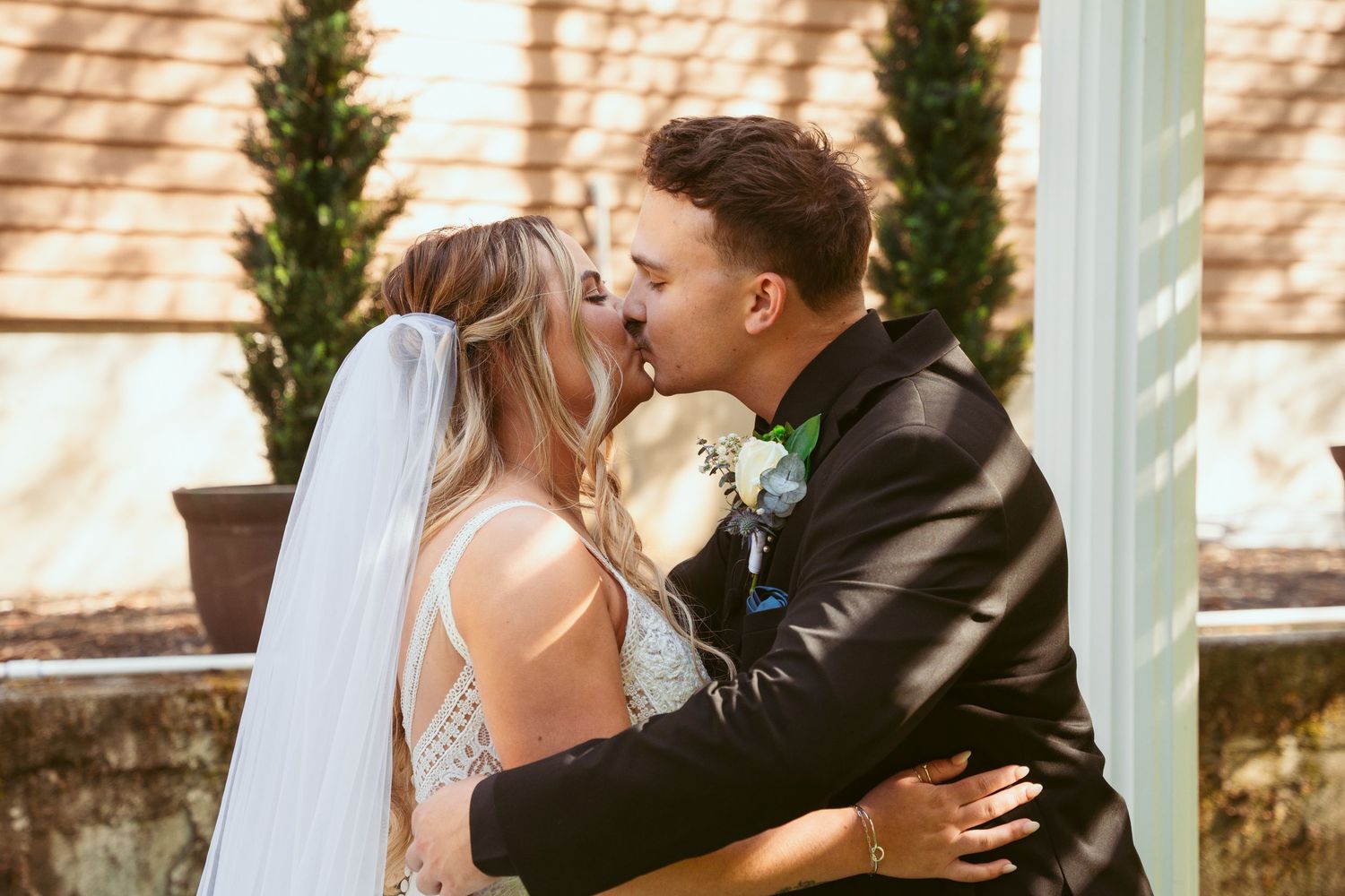 Couple embraces during emotional wedding ceremony moment under white garden pergola.