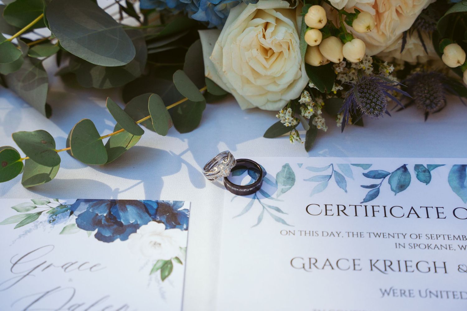 Wedding reception table decorated with white roses, eucalyptus greenery and elegant place settings.